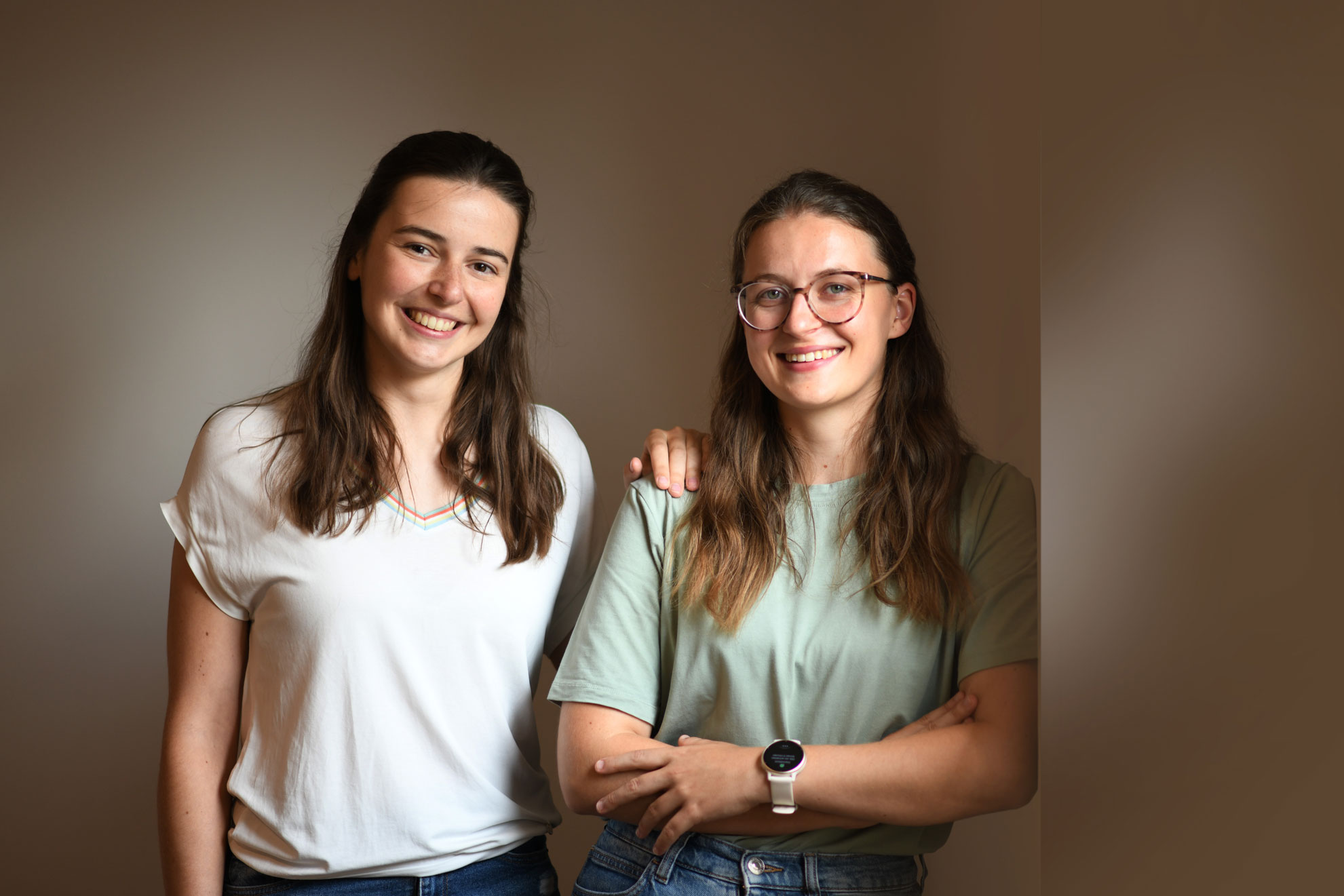 Twee jonge vrouwen staan naast elkaar en glimlachen vriendelijk in de camera.